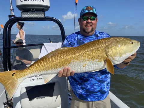 Angler in a blue shirt holding a bull redfish beside the boat's console near Venice, Louisiana