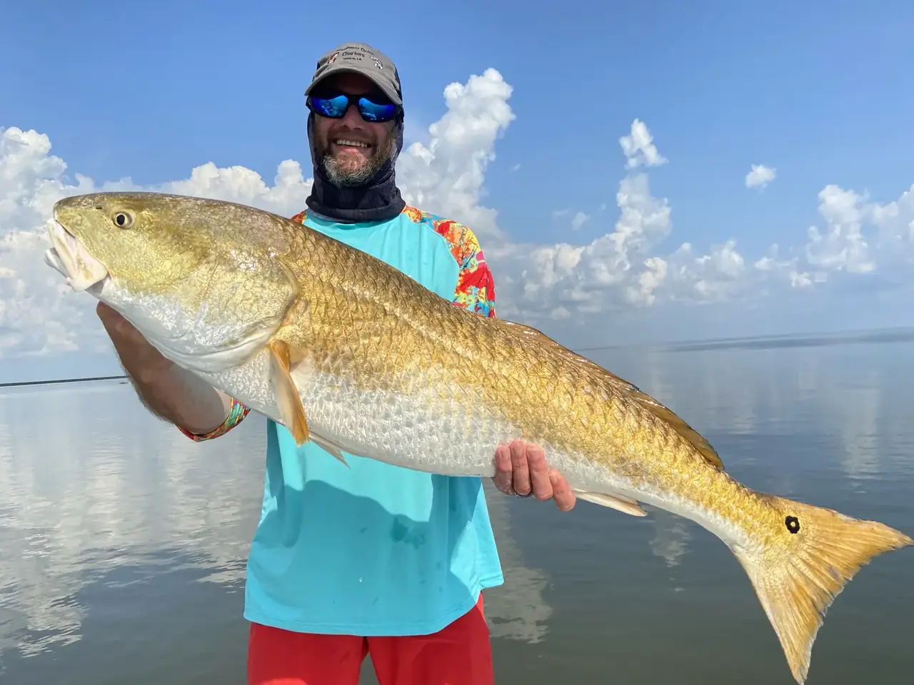 Angler holding a bull redfish over glassy water with clouds on the horizon near Venice, Louisiana