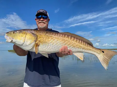 Angler in a Southern Delta Charters cap holding a bull redfish over calm water under a blue sky near Venice, Louisiana
