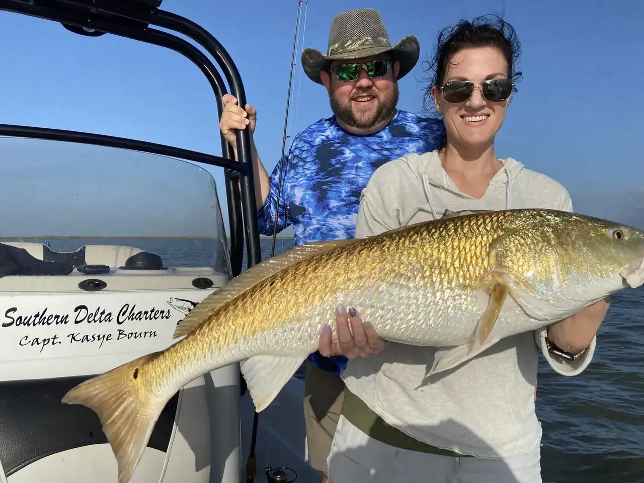 Two anglers holding a bull redfish beside the console lettered Southern Delta Charters, Capt. Kasye Bourn