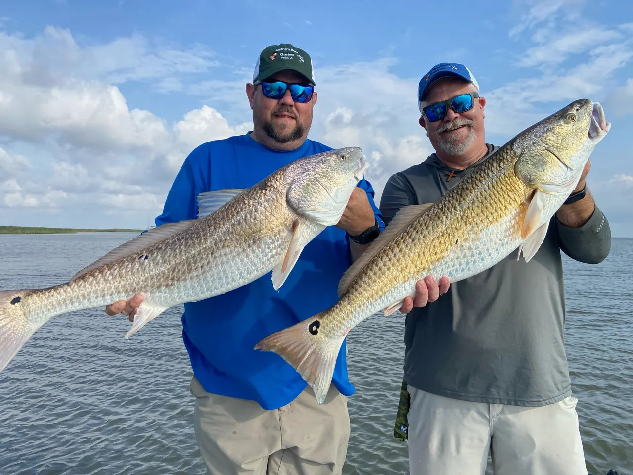 Two anglers in Southern Delta Charters caps each holding a bull redfish on open water