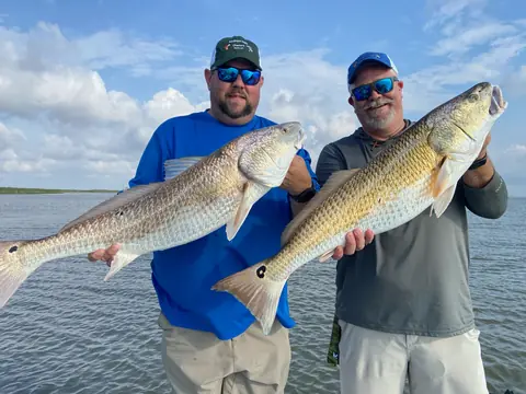 Two anglers in Southern Delta Charters caps each holding a bull redfish on open water near Venice, Louisiana