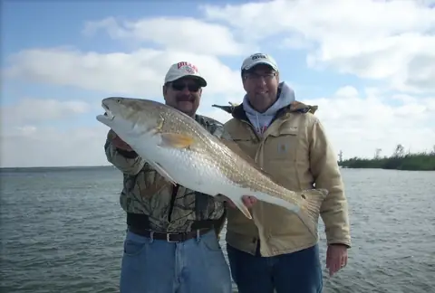 Two anglers holding a bull redfish with marsh behind