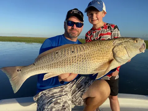 A young angler and an adult holding a bull redfish on the boat at sunrise near Venice, Louisiana