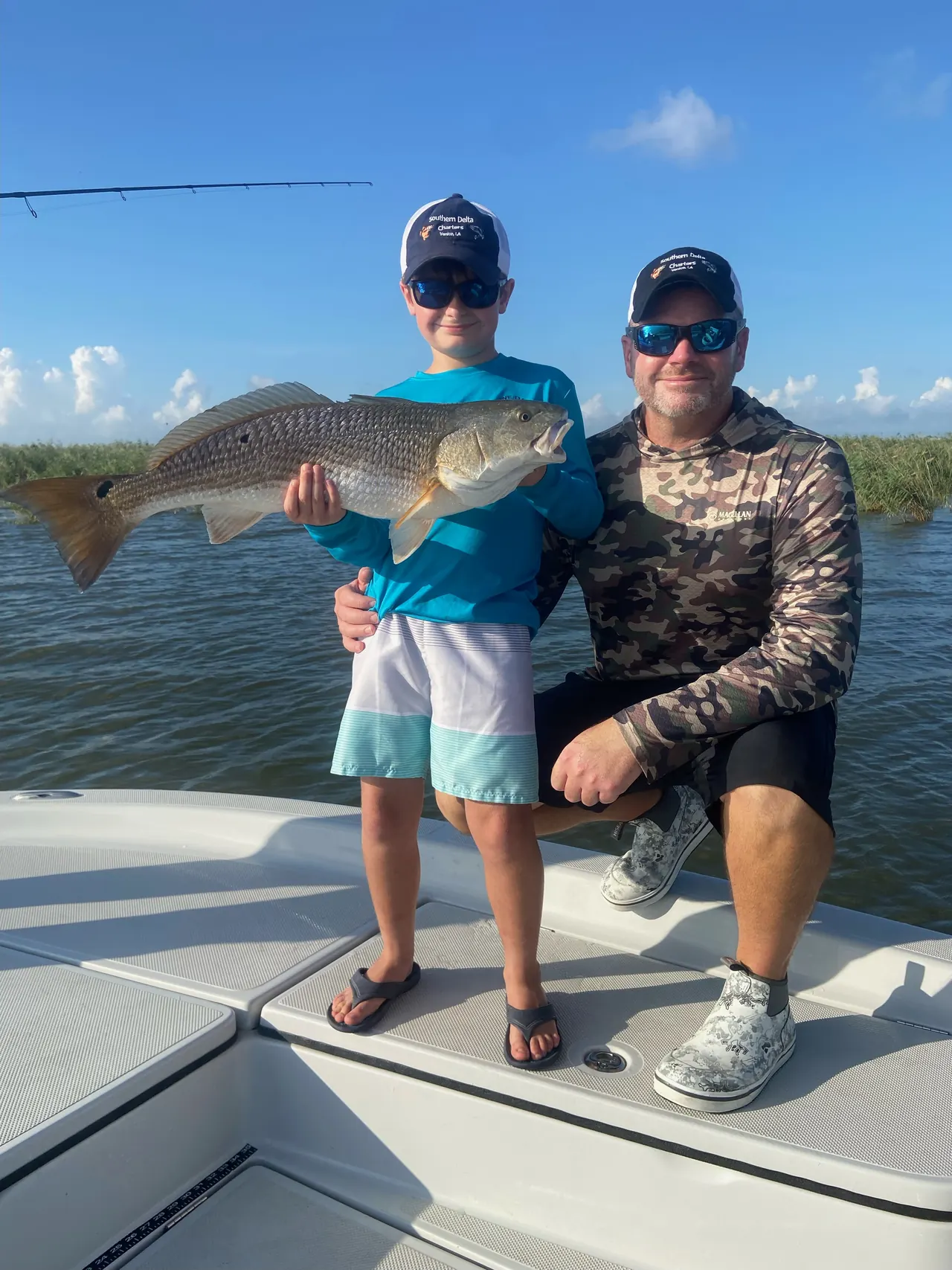 Captain Kasye Bourn kneeling on the bow beside his son, who is holding a redfish