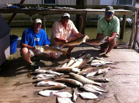Three anglers at the dock with a day's catch of redfish and speckled trout laid out