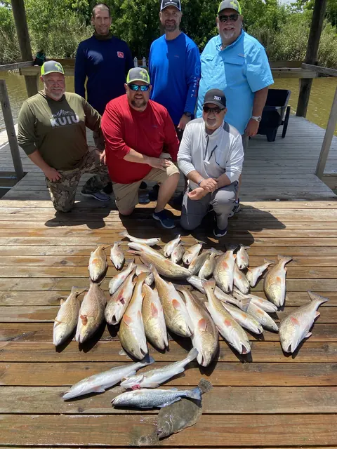 Six anglers behind a catch of redfish laid out on the dock in Venice, Louisiana
