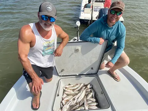 Two anglers kneeling beside a fish box of speckled trout on the bow