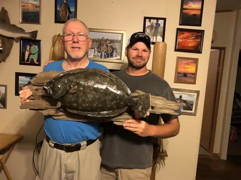 Two men holding a mounted flounder on a piece of driftwood