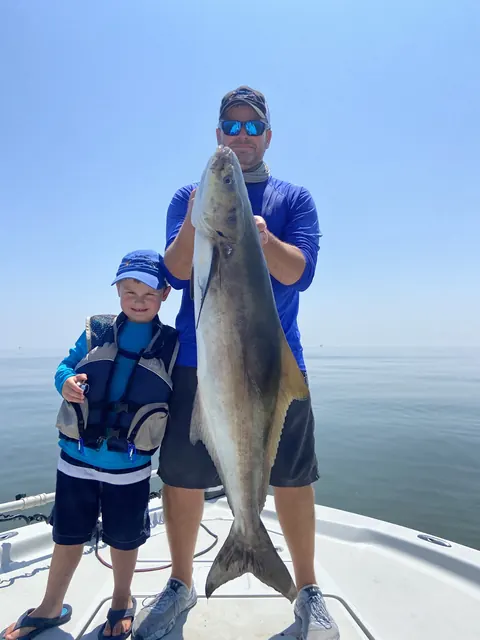 An adult holding up a large fish beside a young angler in a life jacket near Venice, Louisiana