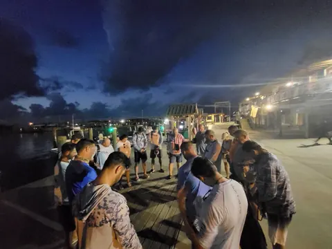 Guests standing in a circle with heads bowed on the dock at Venice Marina before dawn