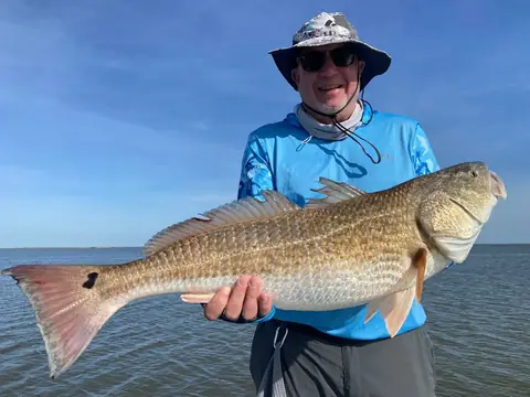 Angler in a bucket hat holding a redfish with a spot on its tail near Venice, Louisiana