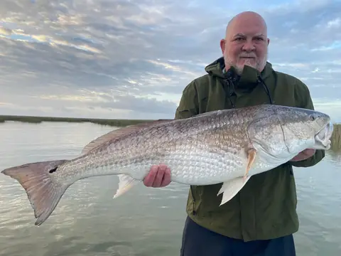 Angler in a green jacket holding a large redfish on a calm morning near Venice, Louisiana