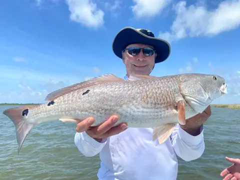 Angler in a wide-brim hat holding a redfish toward the camera near Venice, Louisiana
