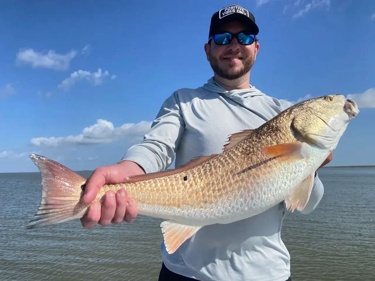 Angler holding out a redfish under a blue sky on open water near Venice, Louisiana