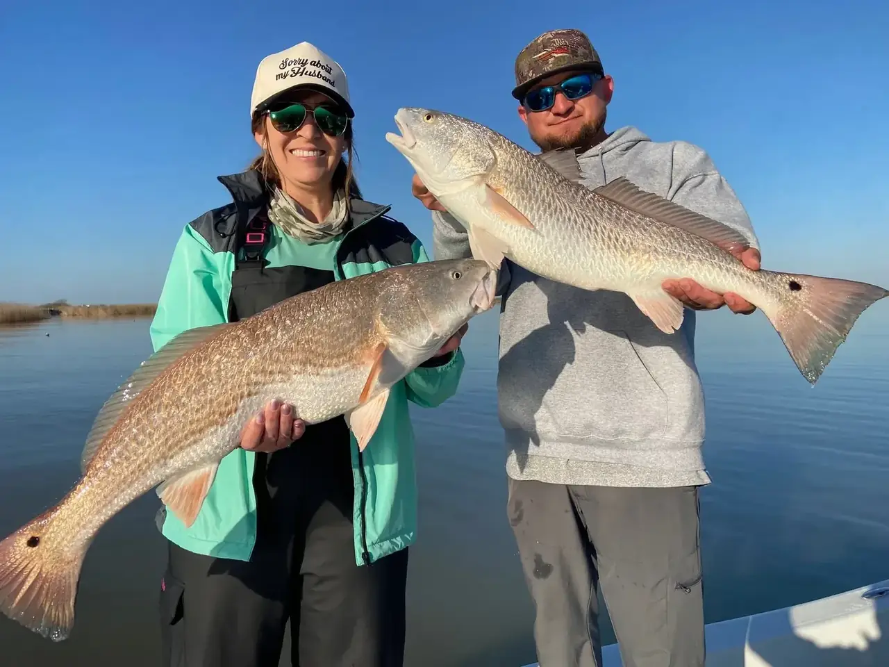 Two anglers each holding a redfish on the boat