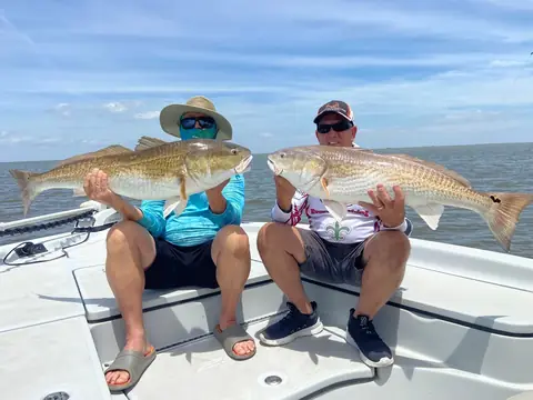 Two anglers seated on the bow, each holding a redfish