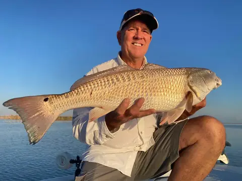 Seated angler in a white shirt holding out a redfish under a clear sky near Venice, Louisiana