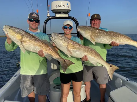 Three anglers each holding a redfish in front of the boat's console near Venice, Louisiana