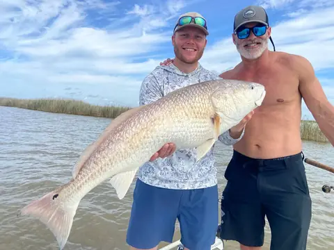 Two anglers holding a redfish with marsh grass behind them near Venice, Louisiana