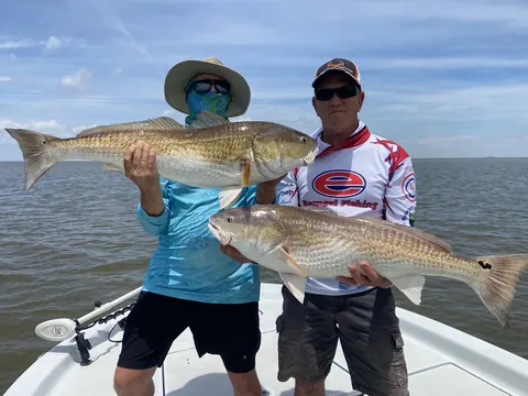 Two anglers on the bow each holding a redfish over open water near Venice, Louisiana