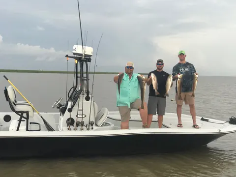 Three anglers holding redfish on the Southern Delta Charters bay boat, seen from across the water