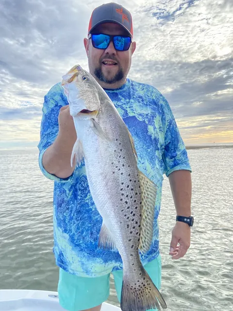Angler in a blue shirt holding up a speckled trout near Venice, Louisiana