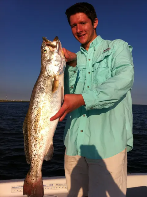 Angler in a teal shirt holding up a trophy speckled trout in evening light near Venice, Louisiana